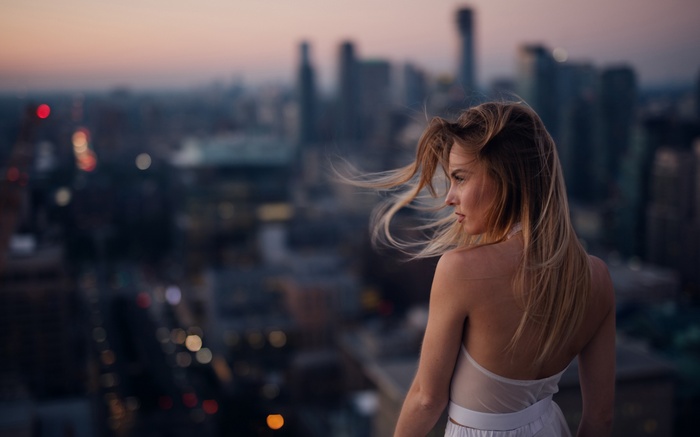 Woman with blonde hair in a white dress overlooking a cityscape
