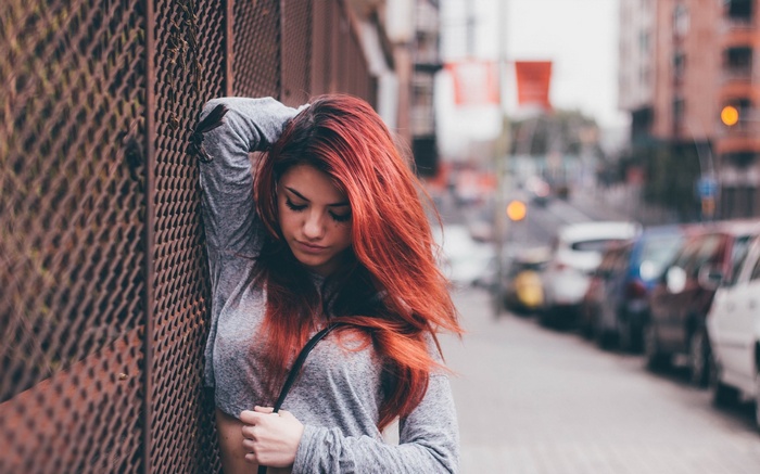 Redhead woman with long hair leaning against a fence