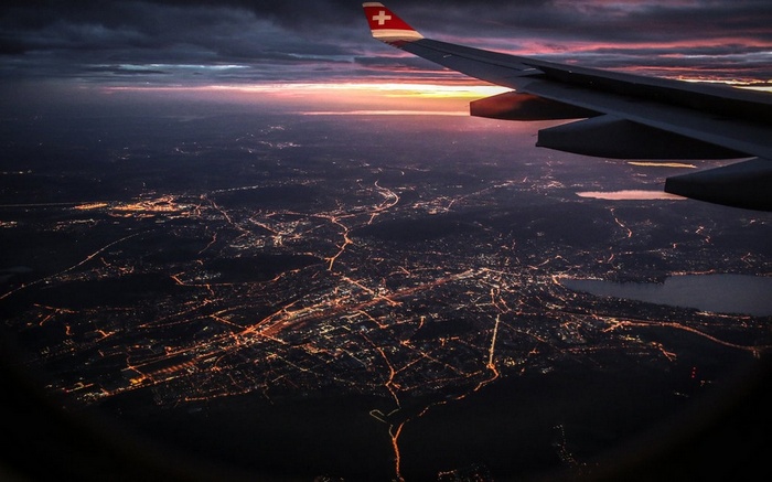 Airplane wing over city lights at sunset