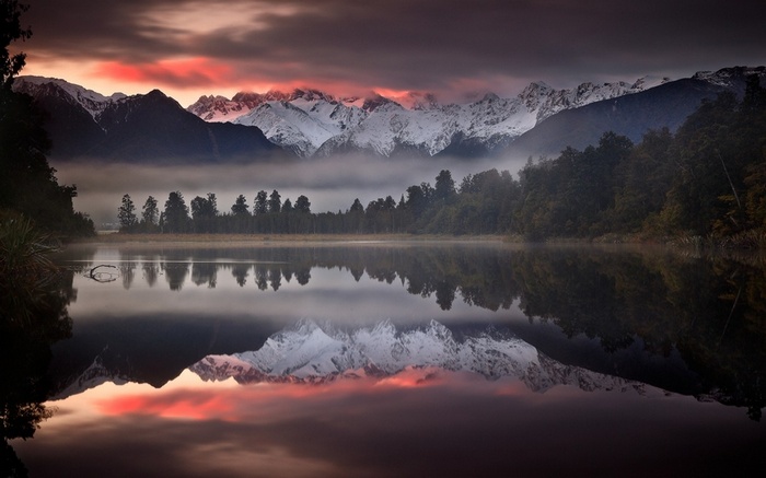 Snowy mountains reflected in a calm lake at sunset