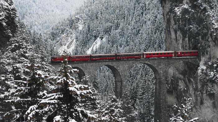 Red train crossing a snowy viaduct in the Swiss Alps