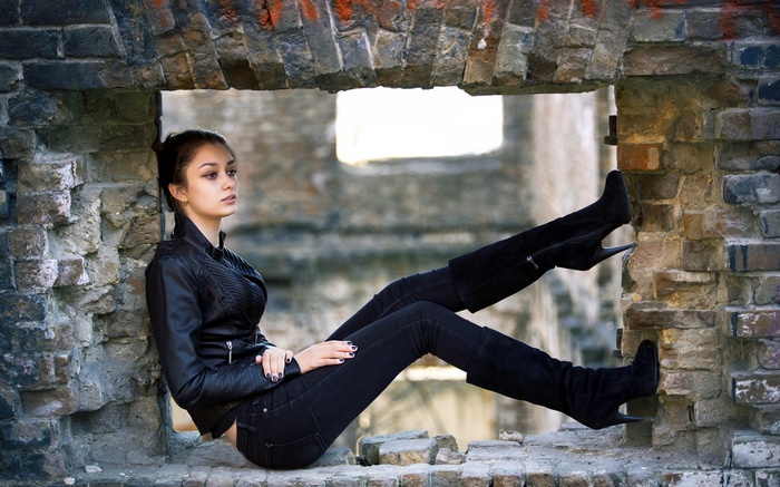 Woman in leather jacket and knee-high boots sitting in ruins