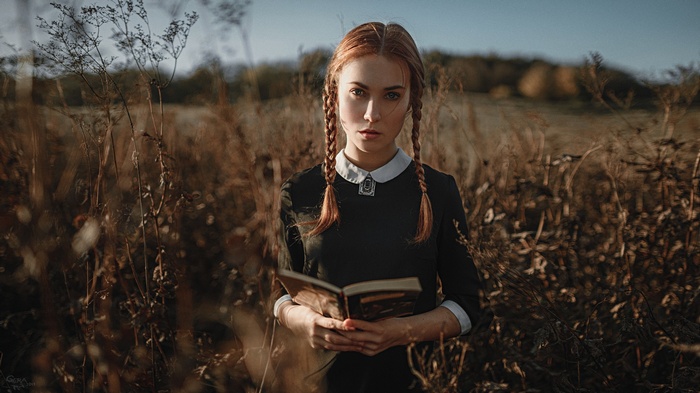 Woman with red pigtails holding a book in a field