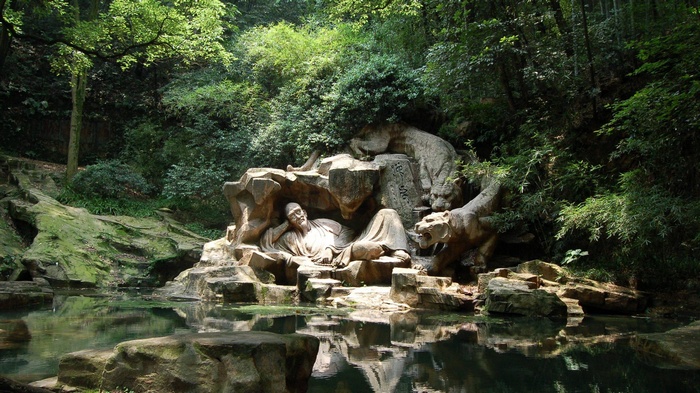 Sculpture of a man and tigers in a forest near water