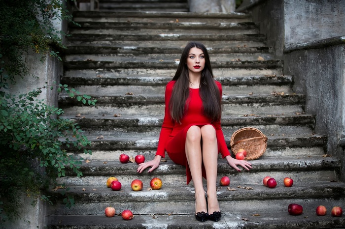 Woman in red dress sitting on stone stairs with apples
