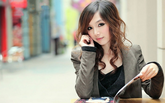 Asian woman with long wavy hair reading a magazine