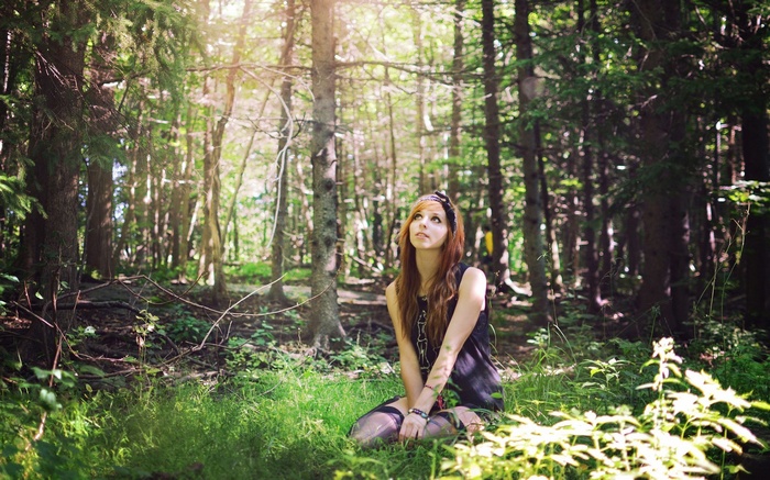 Redhead girl sitting in a sunlit forest