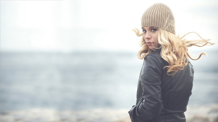 Woman in a beanie and leather jacket by the water