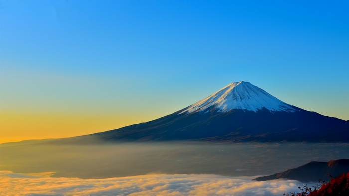 Mount Fuji covered in snow above clouds at sunrise
