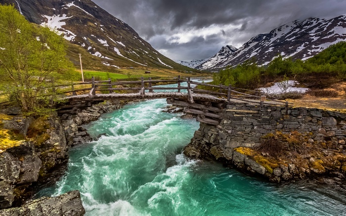 Wooden bridge over a turquoise river in Norway with mountains