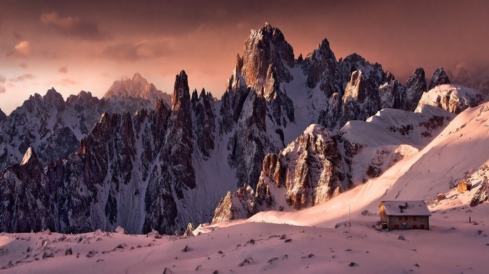 Snowy Alps mountains with a small cabin at sunset