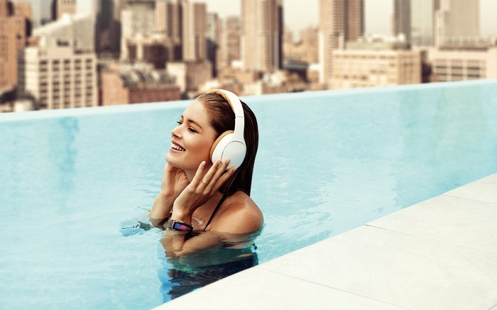 Woman with headphones in swimming pool overlooking cityscape