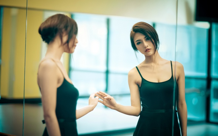 Asian woman in black dress looking in mirror