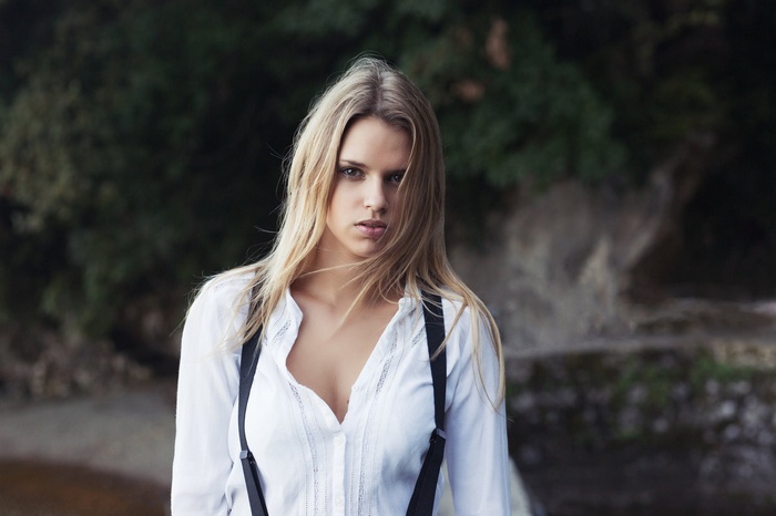 Woman with blonde hair wearing a white shirt and suspenders