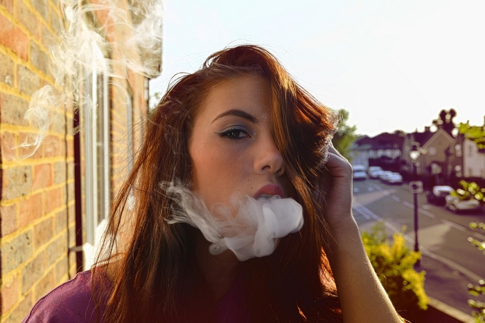 Woman exhaling smoke in front of brick wall