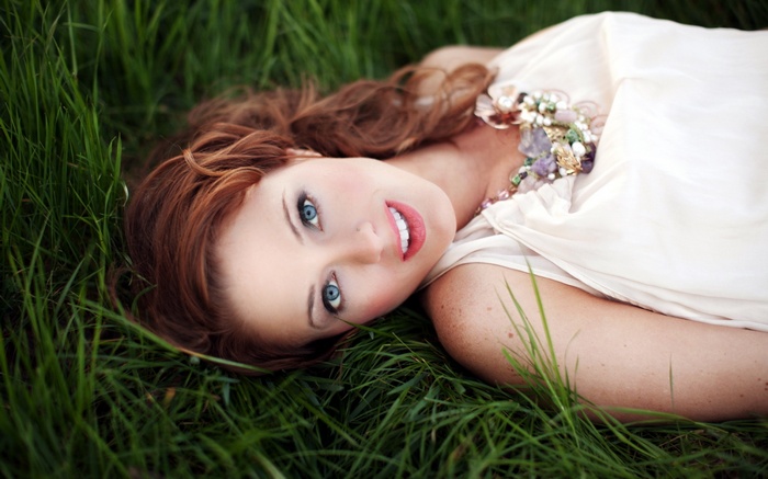 Redhead woman with blue eyes lying in grass wearing a necklace