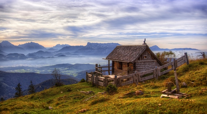 Wooden cabin on a grassy mountain overlooking a misty valley in Austria