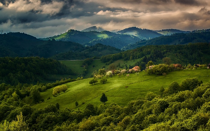 Green rolling hills with houses under a cloudy sky