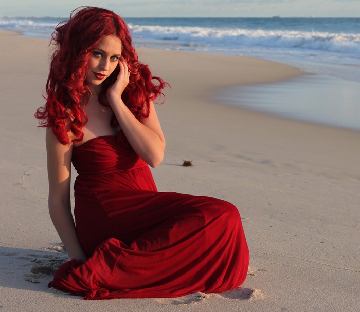 Redhead woman in a red dress on a beach