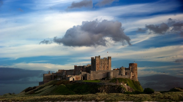 Bamburgh Castle on a grassy hill under a cloudy sky