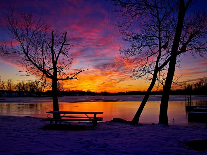 Winter sunset over a frozen lake with trees and snow