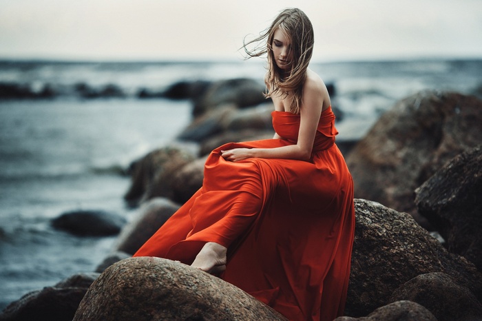 Woman in red dress sitting on rocks by the sea