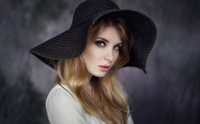 Woman with blonde hair wearing a black hat and white top