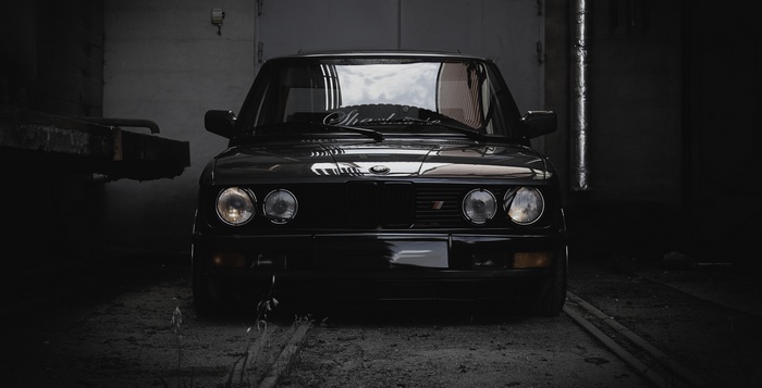 Black BMW E28 parked in a dark garage