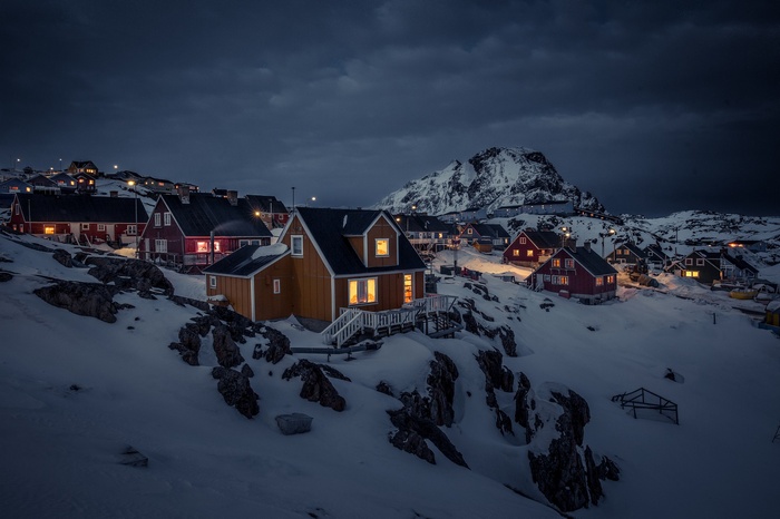 Snowy town in Greenland at night with mountain backdrop