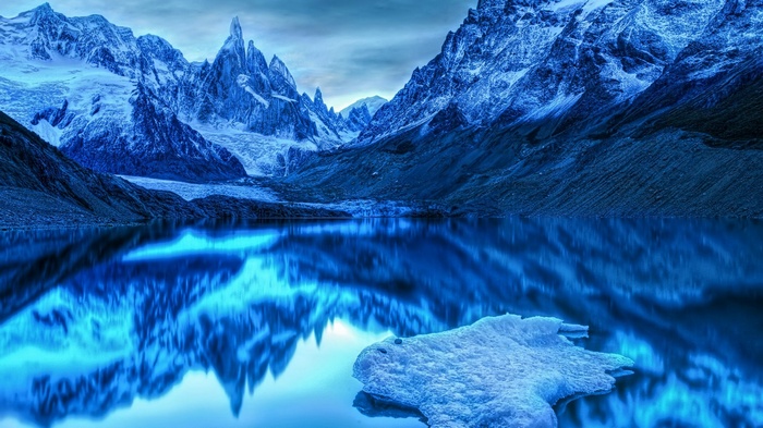 Blue glacial mountains reflected in a lake with ice floe