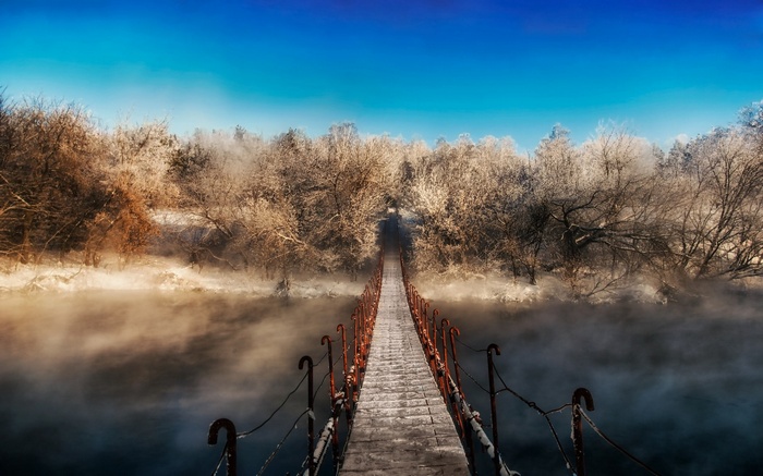 A snowy bridge over a misty river in winter