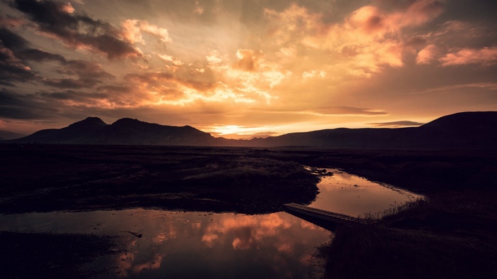 Sunset over mountains with river and bridge reflection
