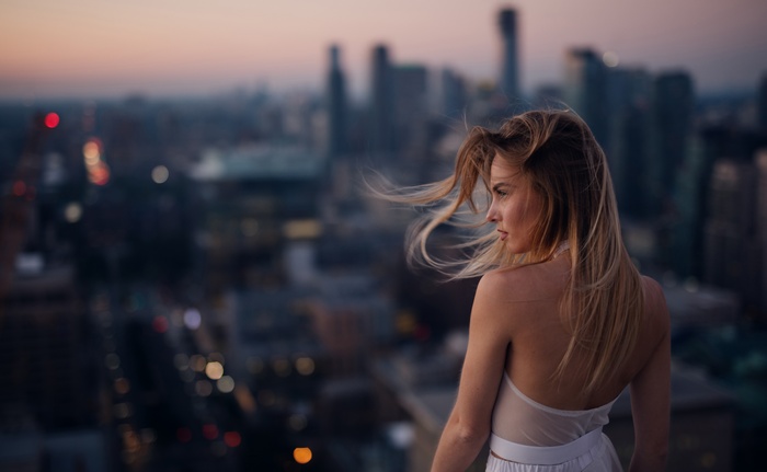 Woman on a rooftop overlooking a city at dusk