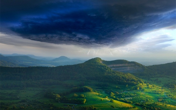 Lightning strikes over green mountains during a storm