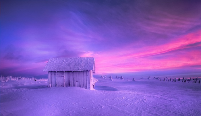 Winter landscape with a snow-covered hut under a colorful sky