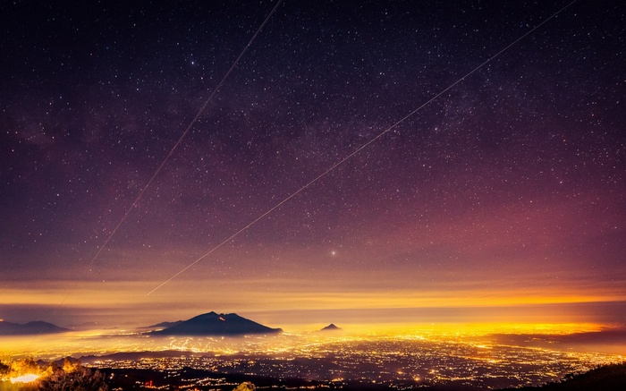 Starry night over a glowing cityscape and mountains
