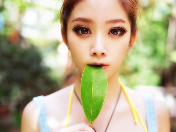 Asian woman holding a green leaf to her mouth