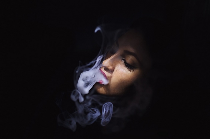 Woman exhaling smoke against a black background