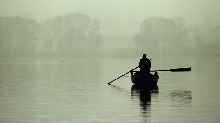 Man in a boat rowing on a misty lake
