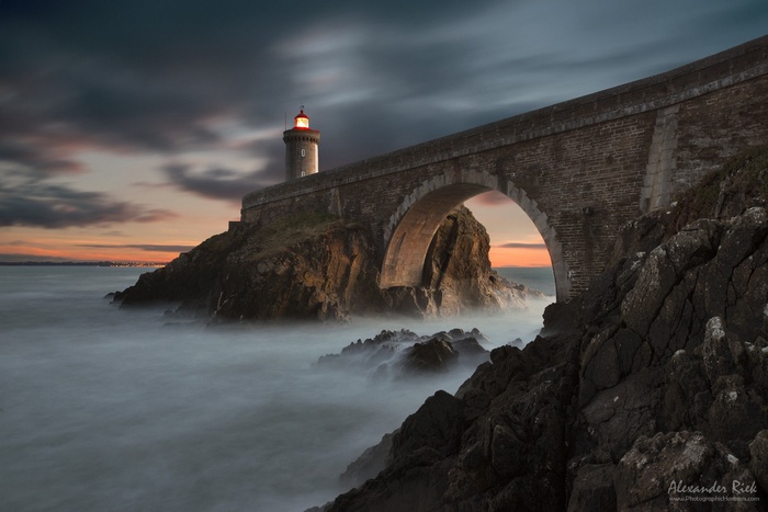 Stone bridge and lighthouse over rocky coast at sunset