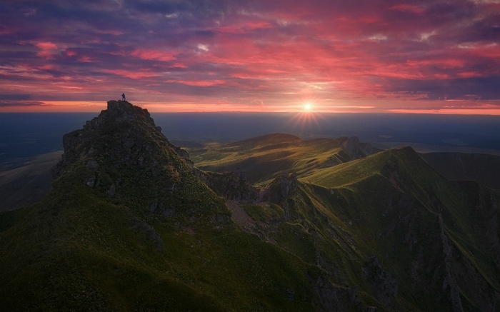 Man on mountain summit at sunset over rolling hills