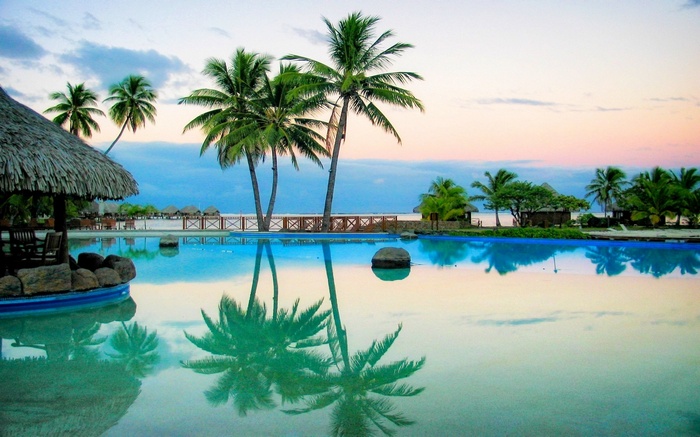 Tropical resort with palm trees and swimming pool at sunset