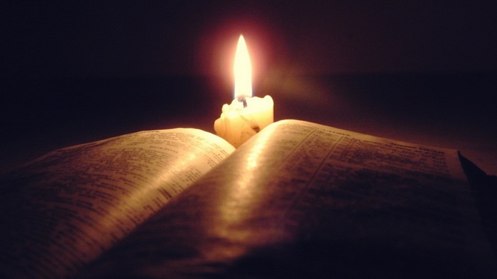 Candle burning on an open Holy Bible