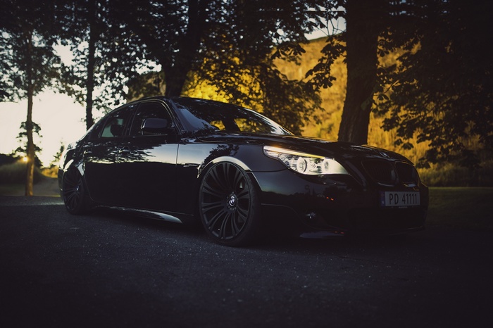 Black BMW E60 M5 parked near trees at sunset