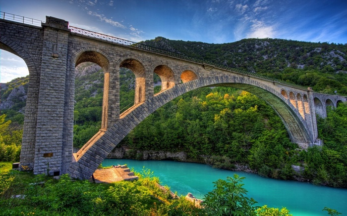 Stone bridge over a turquoise river with green mountains