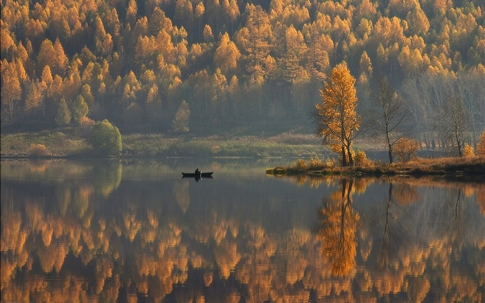 A lone person in a boat on a calm lake with autumn trees reflected