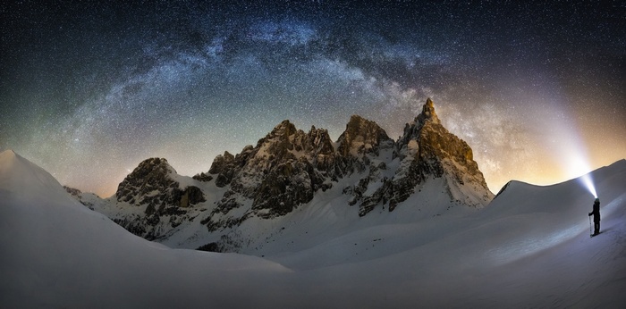 Milky Way over snowy mountains with a person using a headlamp