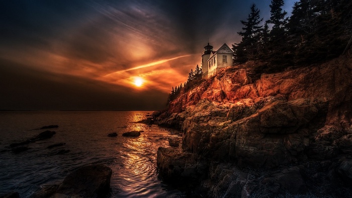 Sunset over a rocky coast with a lighthouse in Maine