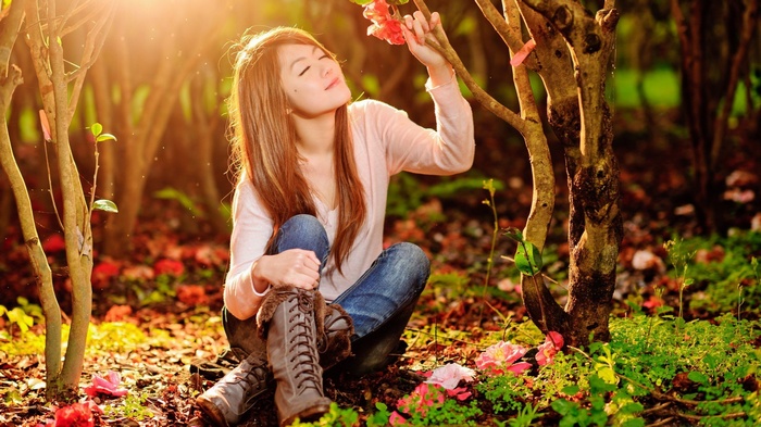 Asian woman in jeans and boots smelling flowers in sunlight