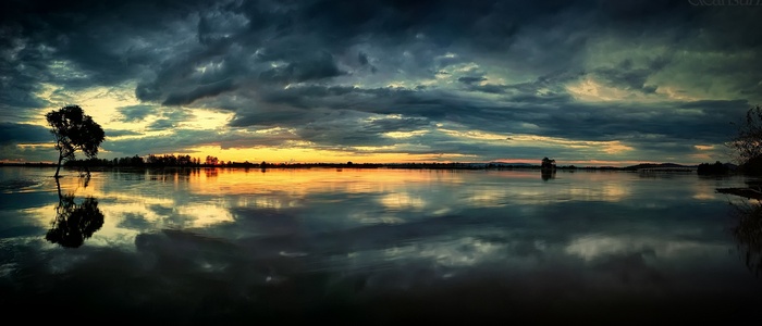 Dramatic sunset over a calm lake with a lone tree